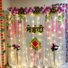 Here is the full view of the simple and elegant Mehndi function decor. The setup includes a beautiful floral border, hanging pink flowers, and tall vases, creating a perfect photo-ready backdrop that is both beautiful and affordable.
