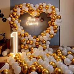 An elegant and romantic first-anniversary decoration. This setup features a large heart-shaped balloon arch in chrome gold and white, a custom 'Happy Anniversary' neon sign, and a light-up number '1', perfect for an intimate and stylish celebration.
