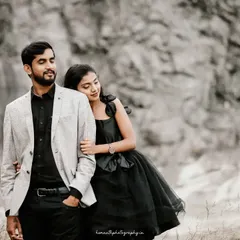 A couple stands against a rugged rock face, sharing a quiet moment. The contrast between their stylish outfits and the raw, natural background creates a striking portrait.