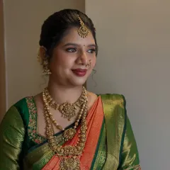 This bride is glowing in her classic South Indian bridal attire. The makeup is focused on creating a smooth, radiant complexion with a defined lip, perfectly matching her green and orange silk saree and antique gold jewellery.