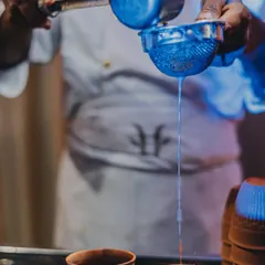 The simple art of making perfect masala chai. A chef strains freshly brewed tea into traditional kulhads, ready to serve guests a warm and comforting beverage, perfect for any weather.