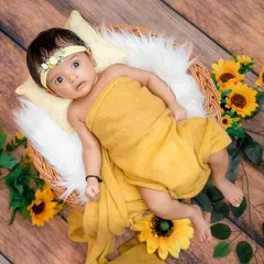 A continuation of the sunflower theme, this shot shows the baby swaddled and lying peacefully in a basket. The wooden floor and bright yellow flowers create a warm, rustic, and cheerful atmosphere.