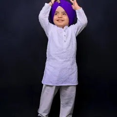 A young Sikh boy in a white kurta and a vibrant purple turban smiles joyfully. This individual portrait, part of a family session, captures his bright and happy personality.