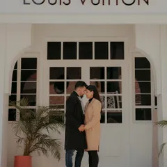 A chic, fashion-inspired shot of a couple holding hands in front of a storefront with European-style architecture, perfect for an urban glam look.