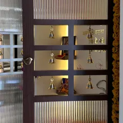 A close-up of a custom pooja room door. The design features frosted glass panels and small cutouts with traditional brass bells, creating a beautiful and spiritual entrance.