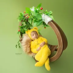 A peaceful newborn portrait of a baby sleeping soundly in a cozy yellow bear outfit. This image showcases my gentle approach to newborn photography, using soft props like a fuzzy blanket and a wooden swing to create a safe and adorable setting.