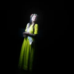 A dramatic, low-key portrait of a bride-to-be during her Mehendi night. The single light source highlights her smile and floral crown, creating an artistic and intimate feel.