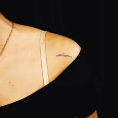 A minimalist mountain range tattoo, perfect for a subtle nod to a love for nature. This fine-line piece is elegantly placed on the collarbone.