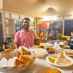 Deepak at our counter, which is full of delicious snacks like samosas and bread pakodas. We are always ready to serve our customers with a smile.