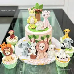 A complete party set for a jungle-themed second birthday. This includes a central cake with adorable, handcrafted fondant animals and a matching set of cupcakes, each topped with a different creature like a lion, elephant, and zebra.