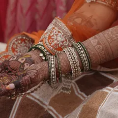 A candid shot from a wedding ceremony, showing the beautiful contrast between the dark mehendi stain and the bride's colorful bangles.