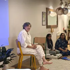 Our founder, Sonya Philip, sits barefoot on a yellow chair, addressing our team. This image captures the grounded, authentic, and reflective nature of our team meetings, where we connect with our core values.