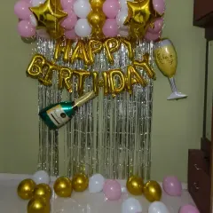 A classic gold, pink, and white home birthday decoration. This budget-friendly option includes a shimmer curtain, foil balloons, and a champagne bottle prop for a fun, celebratory touch.