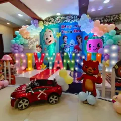 A fun and colorful Cocomelon themed first birthday party, complete with a large backdrop of the characters, marquee letters spelling the name, and a toy car for the little one.