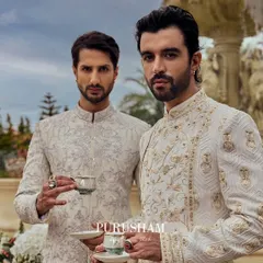 With delicate cups in hand, they embody the spirit of 'Amore'. These two gentlemen wear coordinated but unique ivory sherwanis, showcasing how sophistication can be shared in moments of quiet camaraderie.