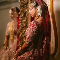 A moment of reflection. This side profile highlights the intricate embroidery on the sleeves and back of the red bridal lehenga, showcasing the detailed craftsmanship.
