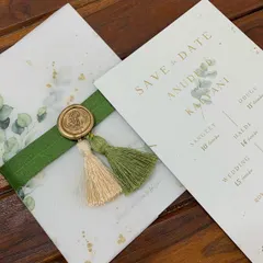This Save the Date card combines a eucalyptus print with elegant gold foil lettering. The card is wrapped in a translucent vellum sheet and secured with a green ribbon, two-toned tassels, and a custom monogrammed wax seal.
