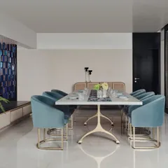 A bright and modern dining area defined by soft blue velvet chairs and a sleek white tabletop. A distinctive blue tiled partition adds a pop of color and texture to the clean, minimalist space.