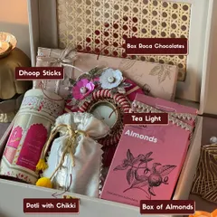 This is my classic 'Gulabi Noor' Diwali hamper, beautifully arranged in a reusable rattan box. It shows exactly what you get, from aromatic dhoop sticks and a decorative tea light to delicious Roca chocolates and chikki-filled potlis.