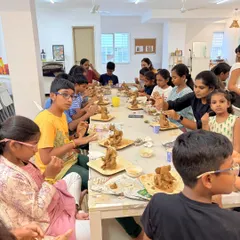 A full table of participants, young and old, deeply focused on sculpting their own clay Ganeshas. It's a perfect family-friendly art activity.