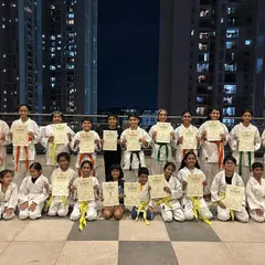 Students from our Prestige Falcon City dojo pose with their new belts and certificates against the Bangalore city skyline, marking a significant milestone in their karate journey.