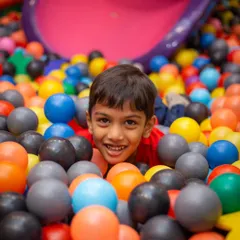 A happy boy peeking out from the ball pit, surrounded by a sea of bright colors. It's the perfect spot for fun photos.
