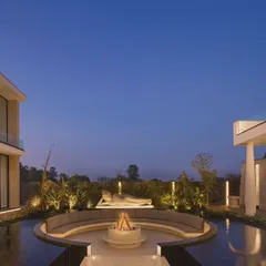 The Ananda courtyard at dusk, where the fire pit glows warmly and the architectural lighting creates a magical ambiance. This space embodies our commitment to creating homes that enhance wellness and provide a peaceful escape.