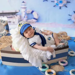 Ready to set sail. This awake and happy baby boy is the captain of his own ship in a fully styled nautical scene, featuring a boat prop, sailor suit, and beach-themed details.