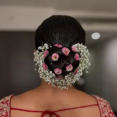 A dreamy combination of pink pom-pom flowers and delicate baby's breath creates a halo effect around this classic bridal bun. This is a perfect look for a bride who wants a soft, romantic feel.