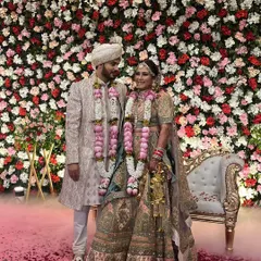 A beautiful couple posing after their Jaimala ceremony. They are standing on a carpet of rose petals in front of a magnificent wall of red, pink, and white flowers.