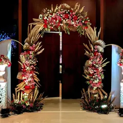A magnificent floral arch designed with red roses and dried pampas grass in golden hues. This statement piece served as a stunning entryway or photo backdrop, blending traditional florals with a touch of modern texture.