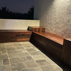 We design and build custom outdoor furniture and seating, like this integrated wooden bench on a stone-paved patio, providing a permanent and stylish resting spot.