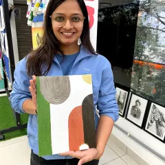 A participant holds up her finished abstract texture painting. In this workshop, you'll learn how to use different tools and pastes to create unique 3D effects.