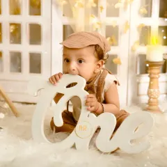 A baby boy celebrating his first birthday with a boho-themed shoot, chewing on a large "One" sign.