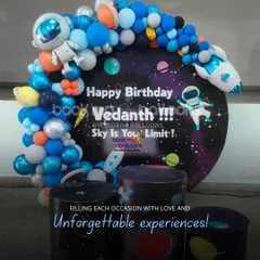 Filling each occasion with love and unforgettable experiences. Vedanth's space party features a circular backdrop with the message "Sky is Your Limit," surrounded by a balloon galaxy of planets and stars.