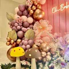 A detailed shot of the enchanted garden decor, highlighting the mix of metallic and pastel balloons, dried palm leaves, and artificial flowers. The mushroom props in the foreground complete the woodland theme.