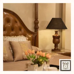 A classic wooden table lamp with a dark finish adds warmth to this bedside. The rich texture of the wood and the soft light from the black shade create a cozy and inviting ambiance, perfect for unwinding in a traditional bedroom.