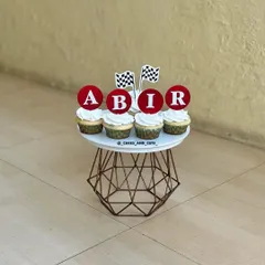 Customized cupcakes for a race car theme, featuring checkered flags and personalized "ABIR" toppers.
