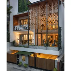 The Screen House at dusk reveals its layered design. The illuminated interiors of the living and bedroom spaces are visible through the intricate screens and large glazing, showcasing a home that balances transparency with the need for privacy in a dense urban setting.