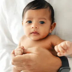 A close-up portrait of a newborn's face, held securely in his father's hands. The focus is on his beautiful eyes and delicate features.
