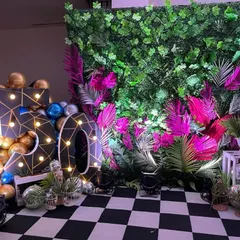 A unique 50th birthday decoration with a checkerboard floor. The setup includes a lush green wall with pink accents and large, stylish marquee numbers.