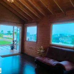 A view from inside the wooden cottage, with the door open to the landscaped terrace, showing the seamless indoor-outdoor connection.