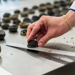 Precision in every detail. A chef carefully places a dark, textured garnish onto a pastry, showcasing the meticulous handwork that goes into our dessert creations.