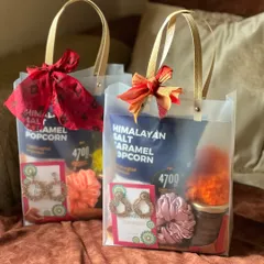 A pair of Rakhi gift bags for sisters. These transparent bags are filled with gourmet popcorn, jewelry, and scrunchies, finished with a festive ribbon.