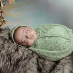 A close-up of the baby in the green vine wreath, resting on a soft fur blanket. The natural elements create a serene and organic feel.