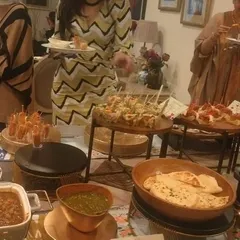 Guests enjoying a high-tea experience. The buffet includes a variety of appetizers on tiered stands, hot snacks like Mattra Kulcha, and an array of desserts.