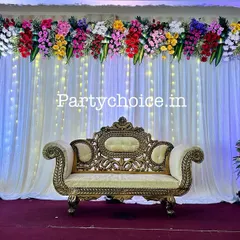 This is a close-up of the stage we designed for a Half-Saree ceremony. The elegant sofa is set against a backdrop of white curtains and fairy lights, with a colorful floral arrangement on top.