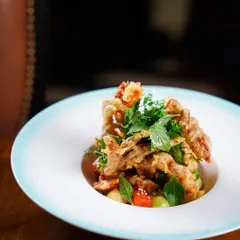 A beautifully plated fine-dining dish of soft-shell crab at The Table, Colaba. The minimalist presentation and restaurant ambiance in the background convey a sense of sophistication and culinary art.