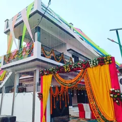 A grand entrance decoration for a wedding house. The gate is decorated with a large arch of yellow and pink drapes and flowers, and the house facade is also adorned with colorful fabric.