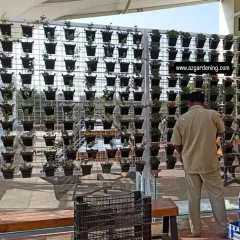 This image shows the framework of a large vertical garden during installation. The metal grid is mounted, and my team is placing each potted plant into its designated spot to create the final design.